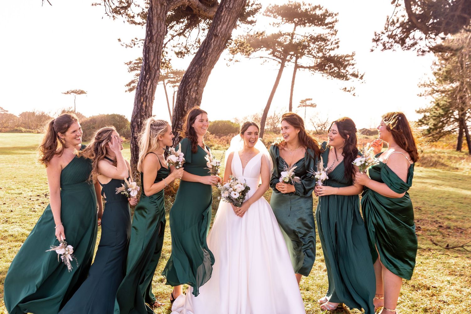 A bridal party in emerald green dresses shares a candid moment outdoors.