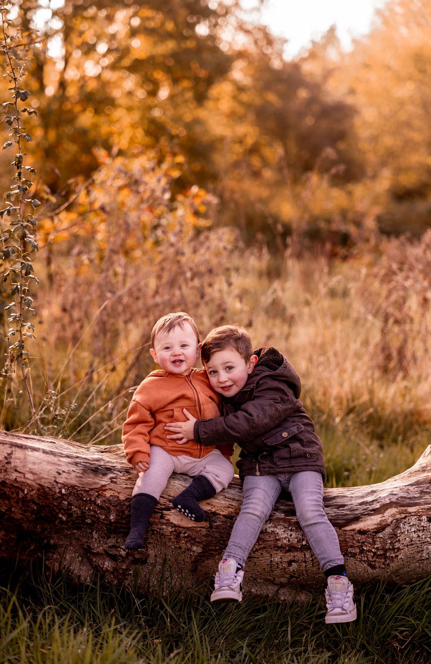 Two children sitting together on a fallen log during golden hour in a natural setting.