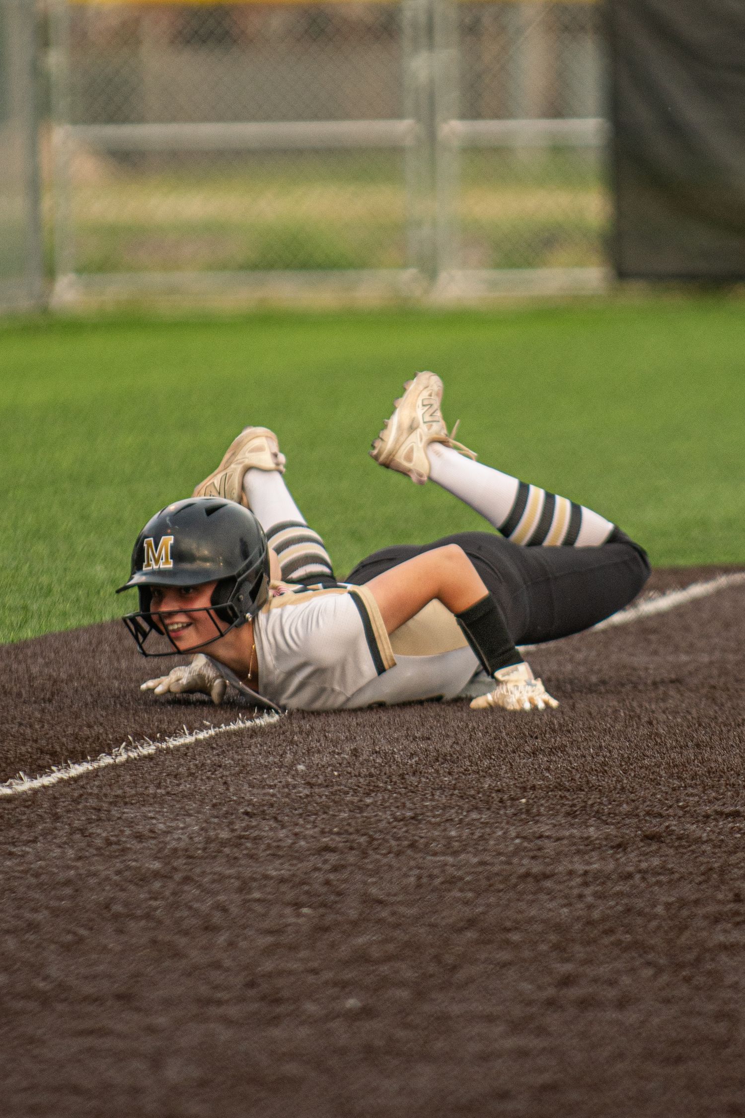 Softball player slides into base wearing black and gold team uniform.