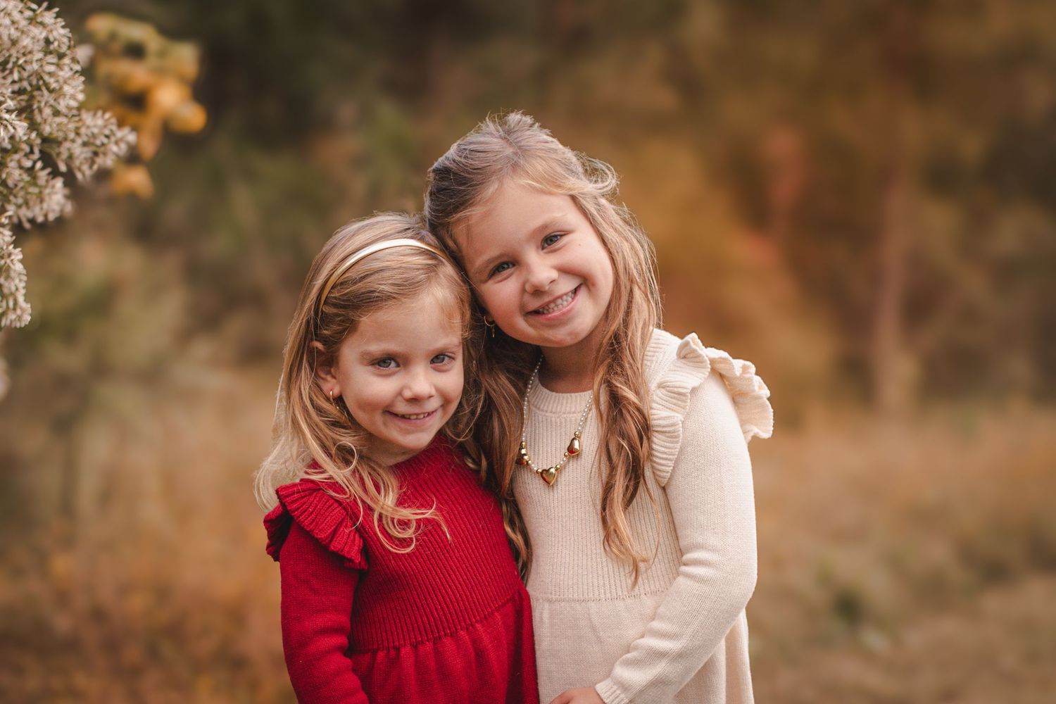 Two young sisters smiling and hugging outdoors in autumn setting.
