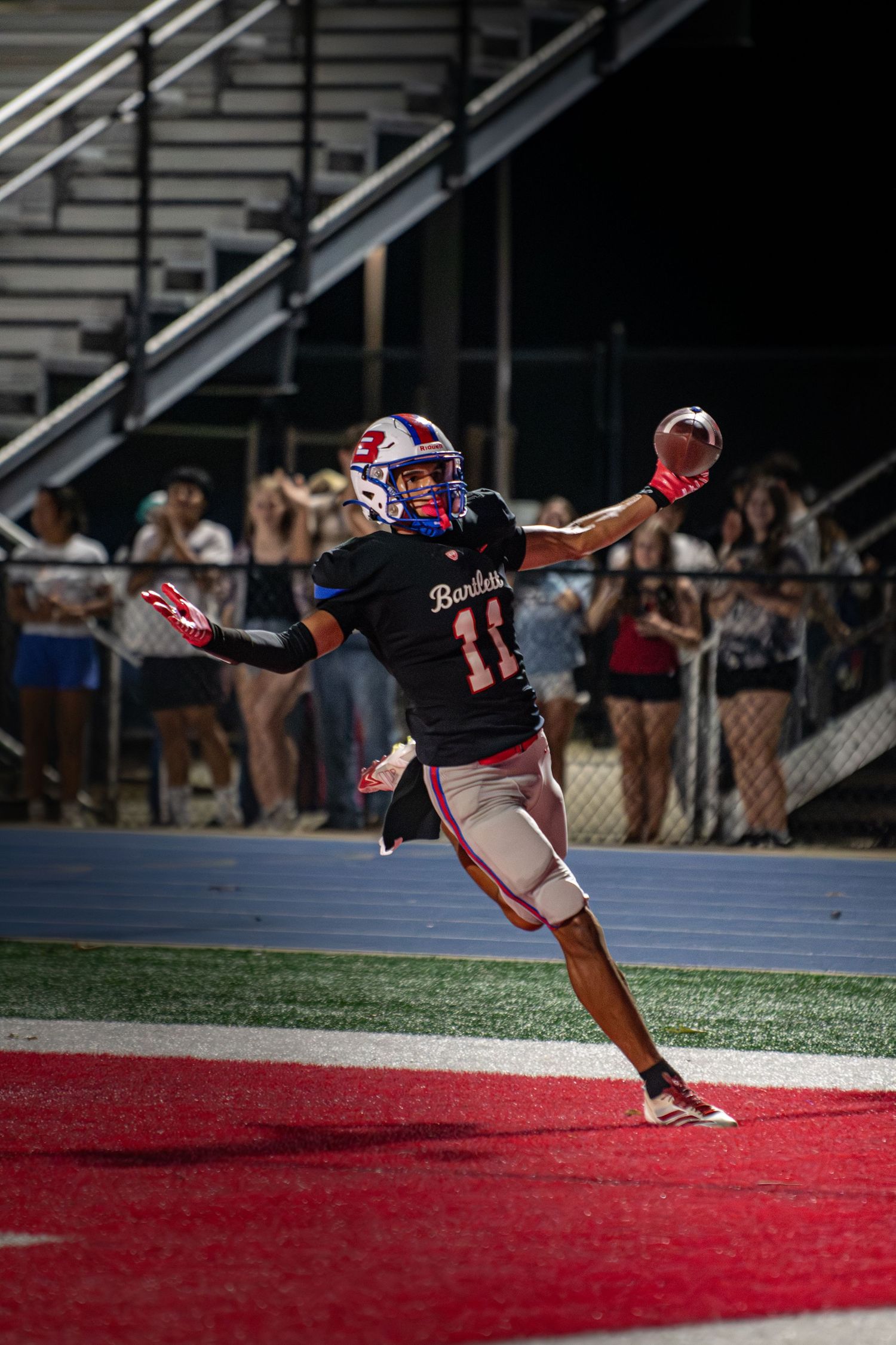 Football player #11 catches a pass in the end zone during a night game at a high school stadium.