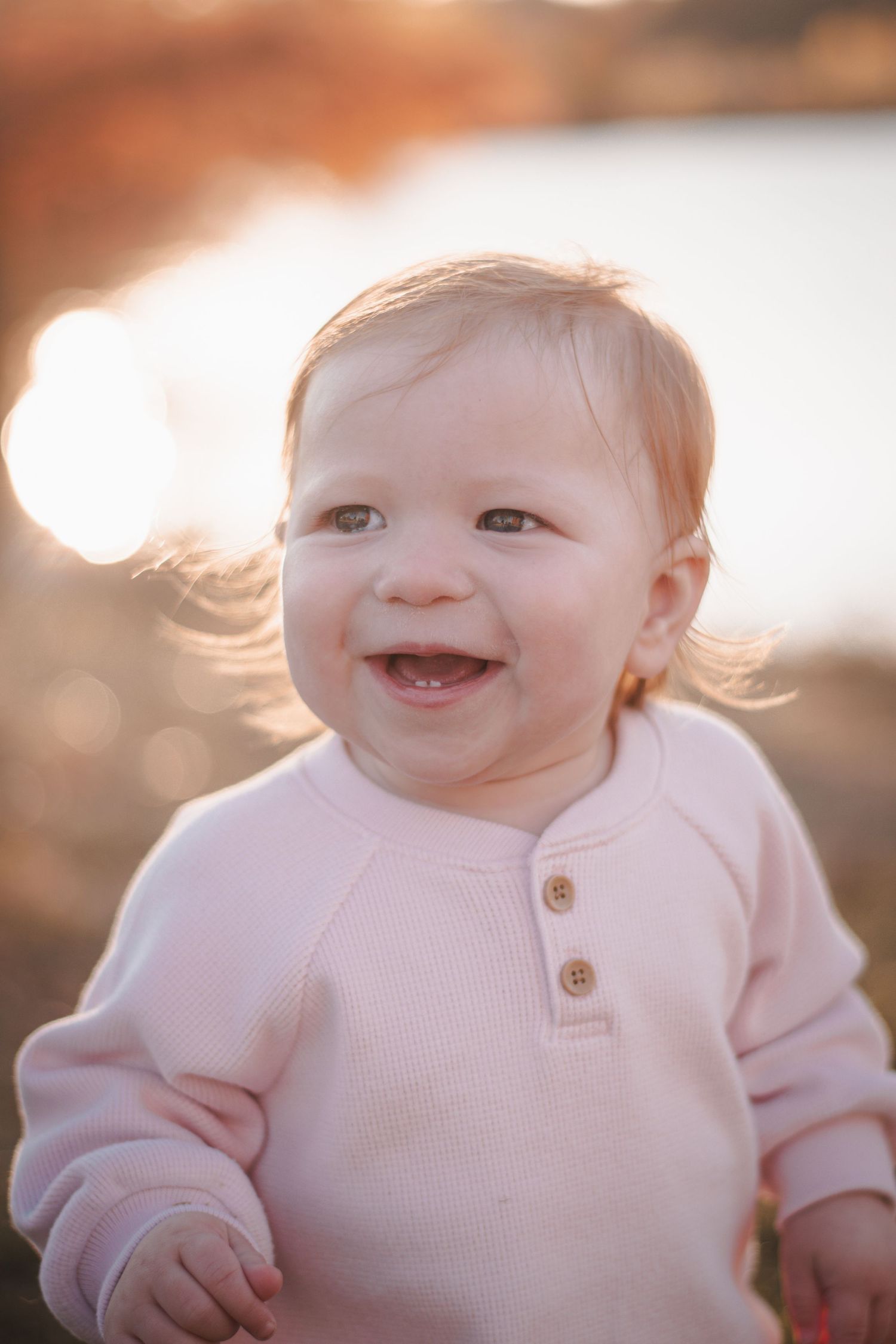 Smiling baby in pink sweater outdoors in golden sunset light.