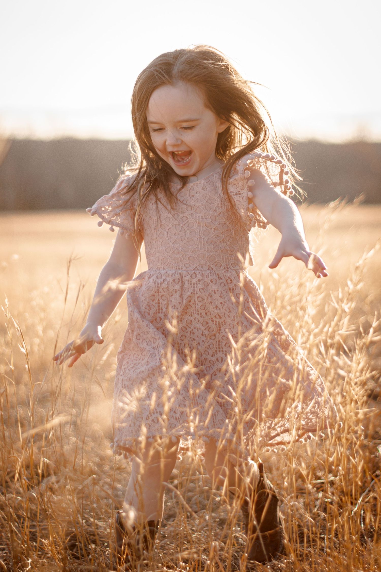 Young girl in pink dress running joyfully through golden wheat field at sunset.