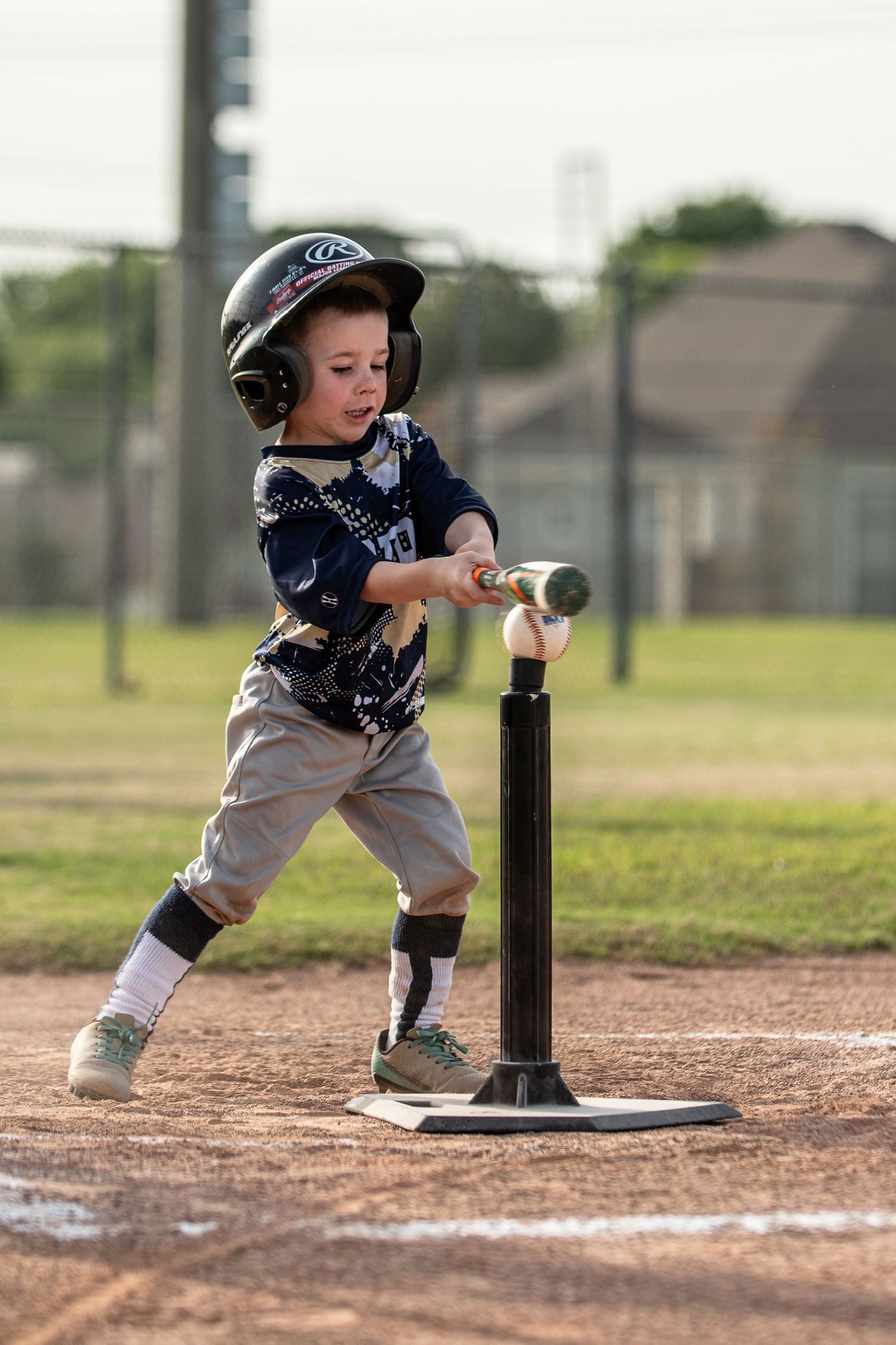 Young toddler in helmet swinging bat at T-ball tee on baseball field.