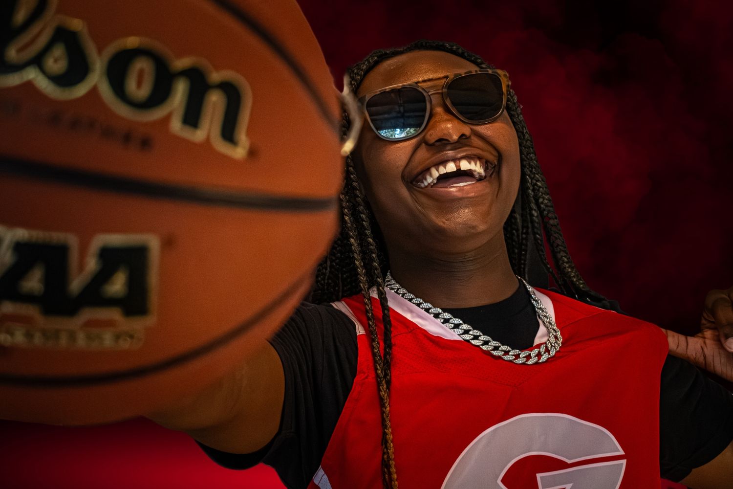 Young basketball player laughing while holding a Wilson NCAA ball wearing sunglasses.