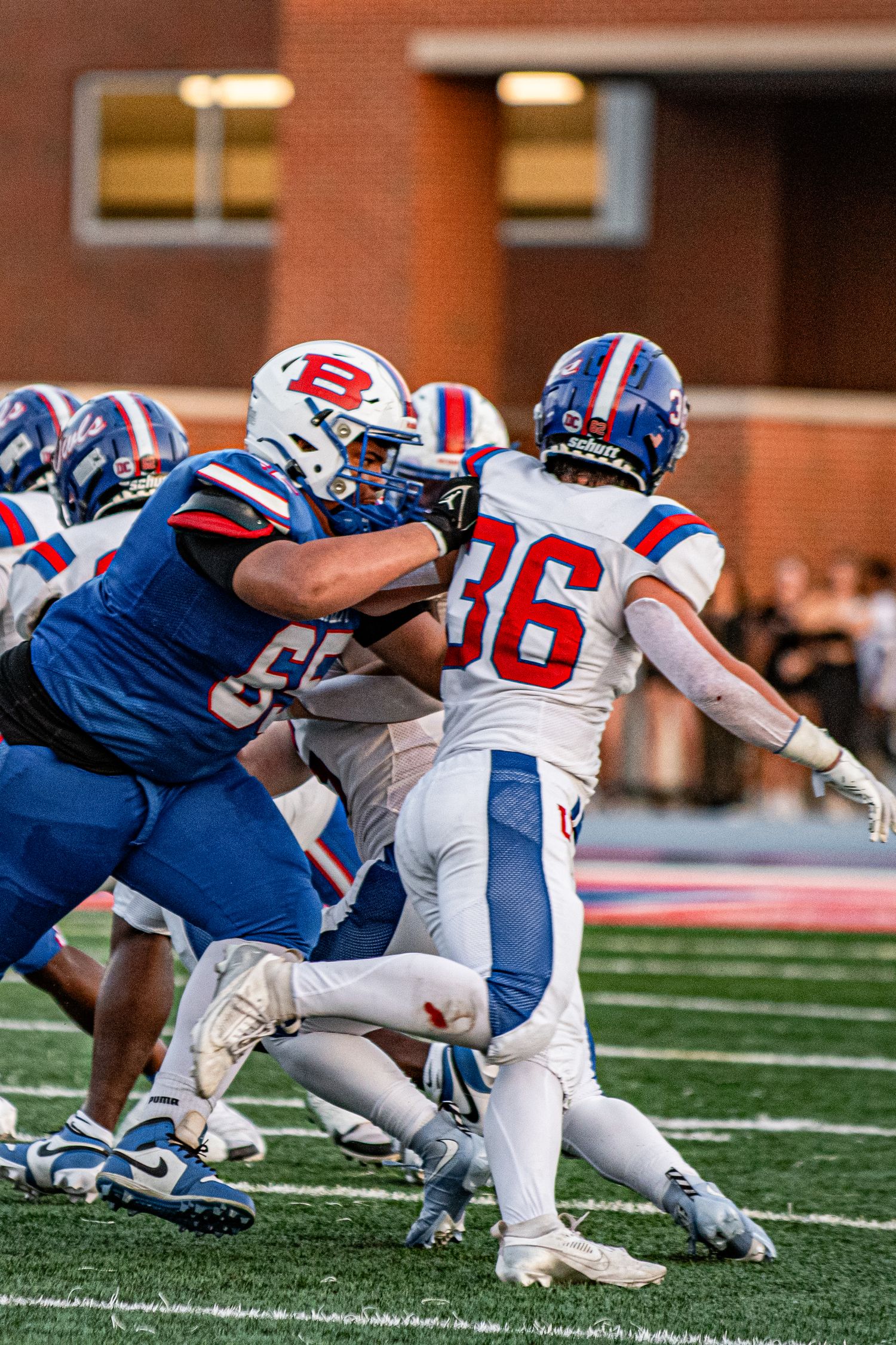 High school football players in blue and white uniforms clash on the field during an intense game-time play. Game day photography.