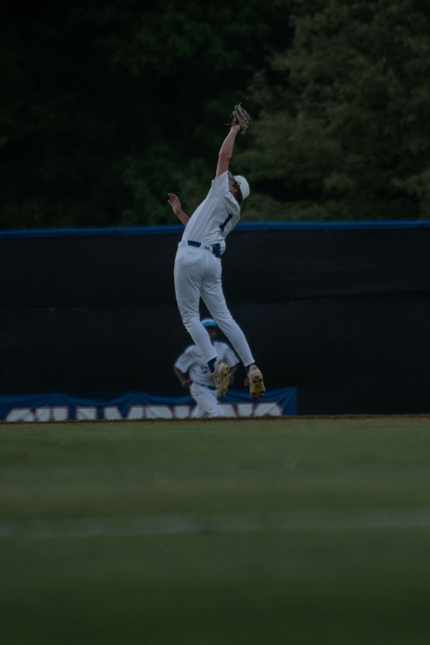 Baseball outfielder jumping to catch fly ball near outfield wall.