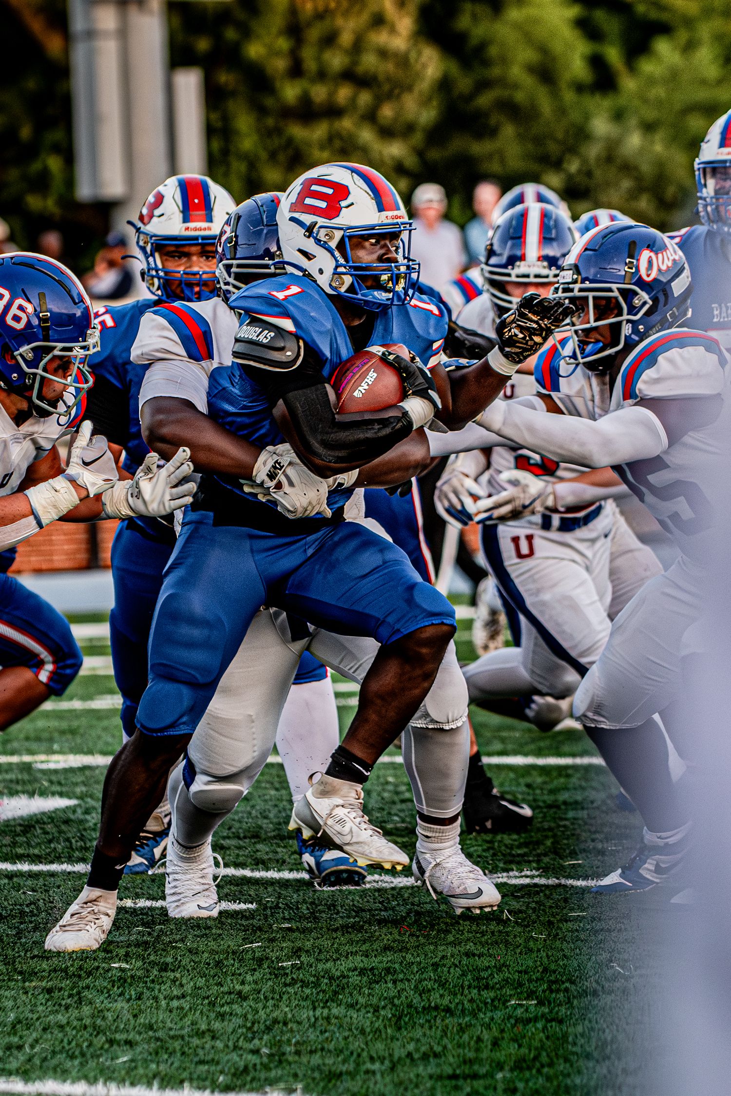 Football players in blue uniforms compete during an intense college football game on a green turf field.