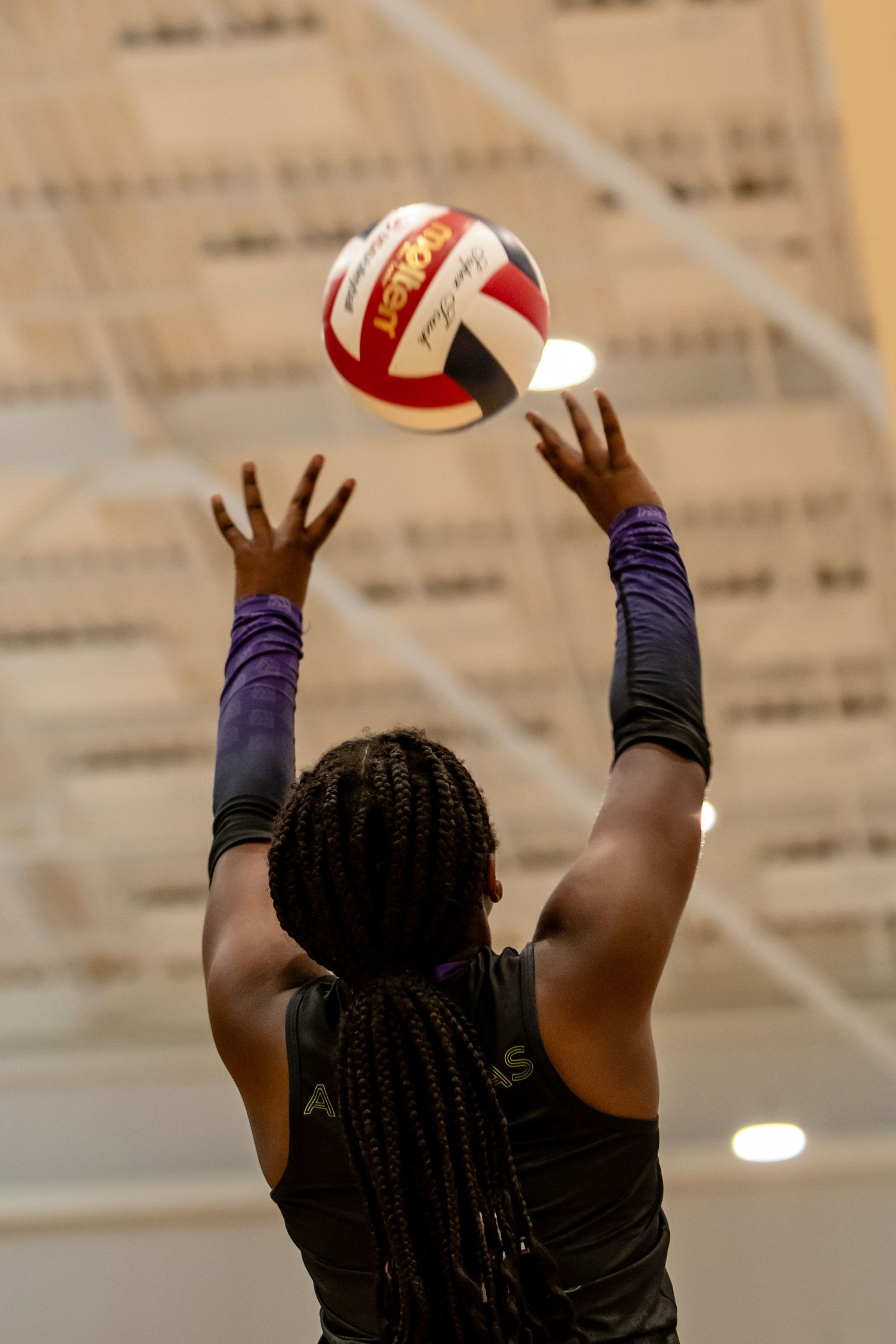 Female volleyball player sets the ball with both hands raised overhead during an indoor game.