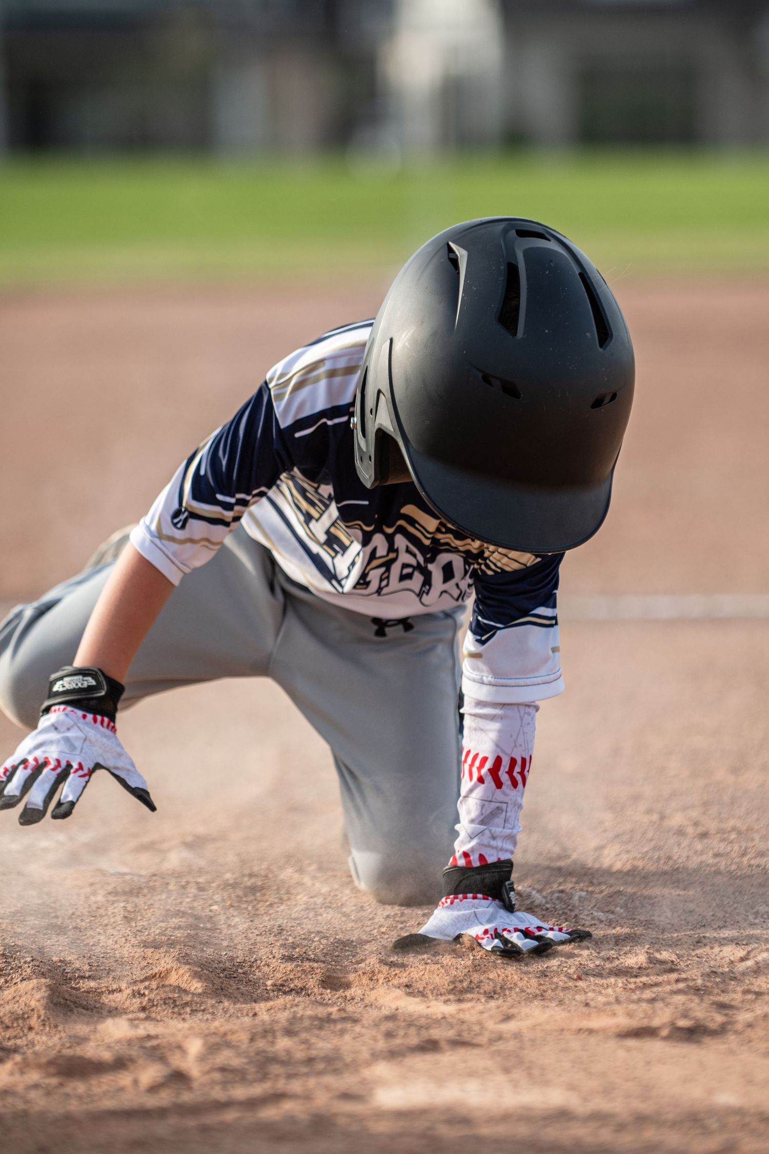 Youth baseball player sliding headfirst into base in cloud of dust.