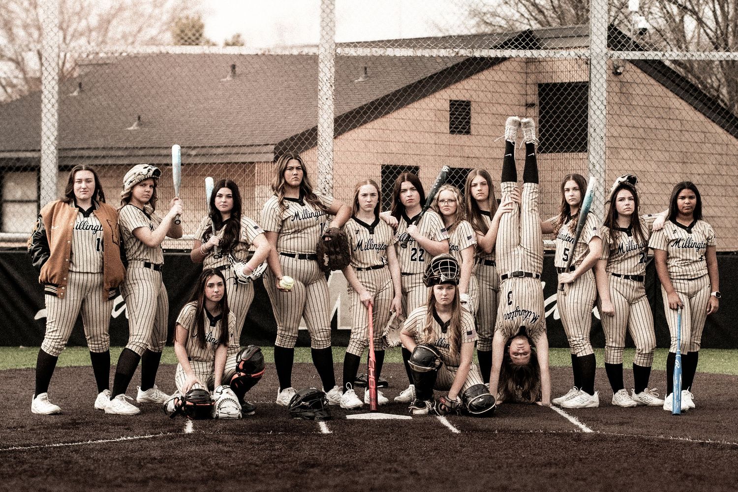 Girls softball team poses together on the field with bats and gloves in uniforms.