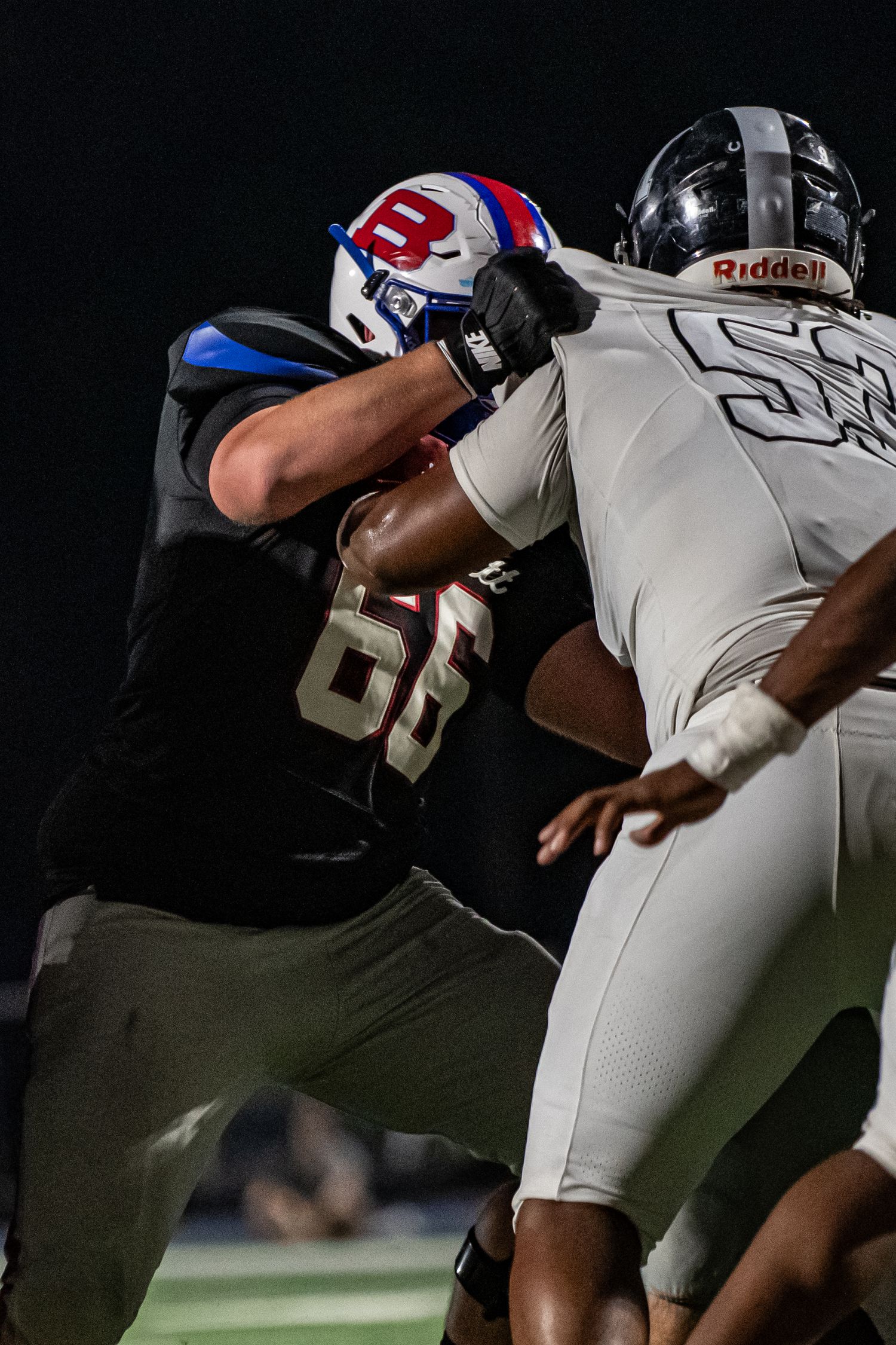 Two football linemen battling at line of scrimmage during night game.