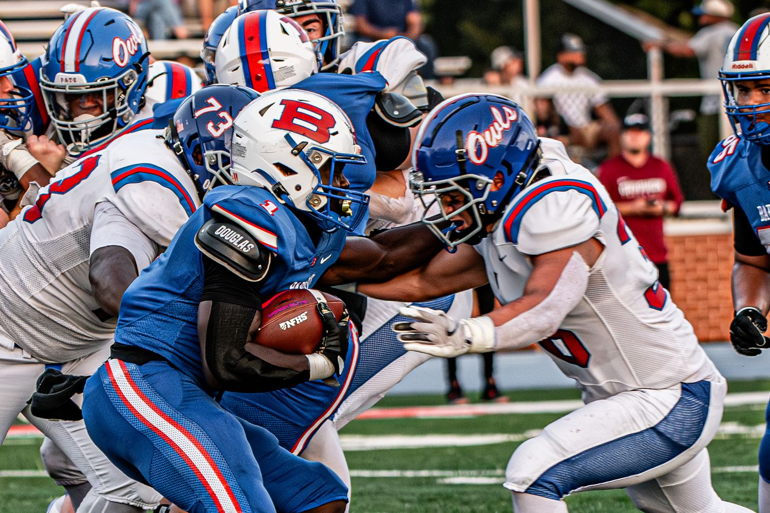 College football players in blue and white uniforms compete during an intense tackle play on a sunny game day.