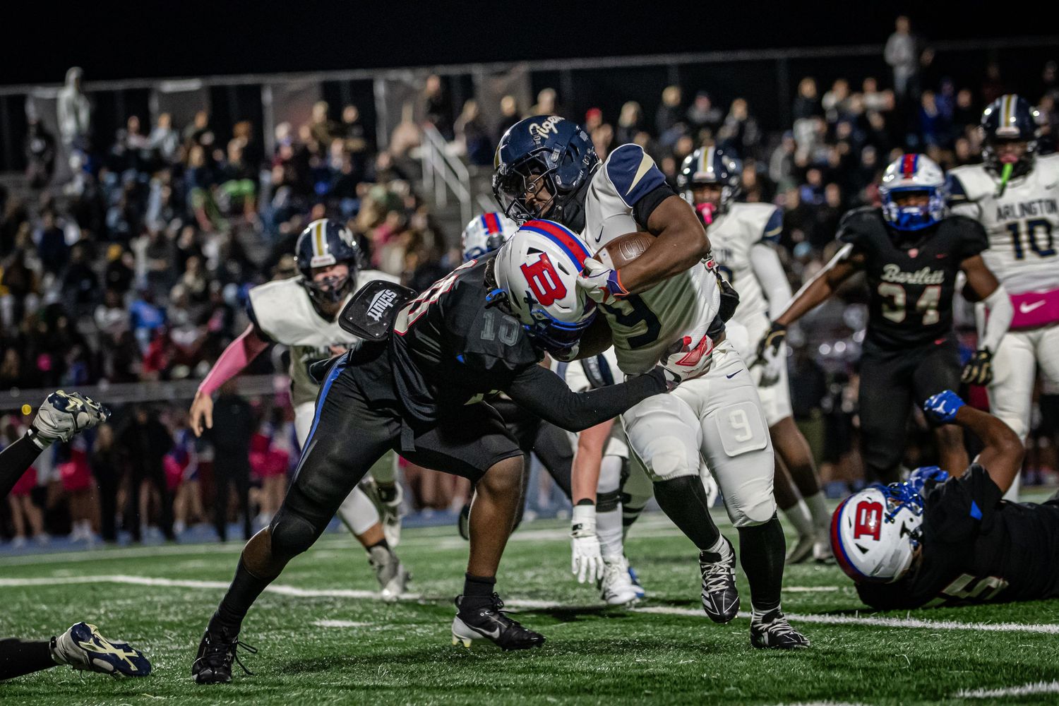 High school football players collide during an intense night game under stadium lights on a well-lit field.