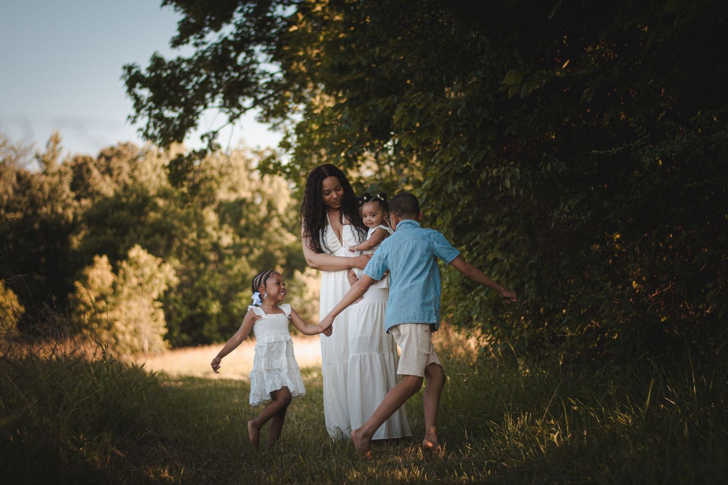 A family of three enjoys a golden hour moment in a lush green meadow, with children playing around their mother.
