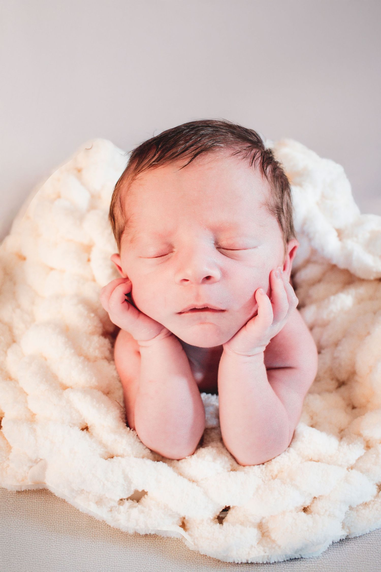 Peaceful newborn baby sleeping with hands on cheeks on a soft white blanket.