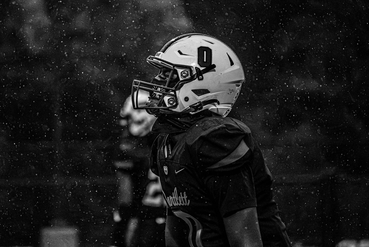 Black and white photo of a football player wearing helmet number 9 standing in the rain during a game.