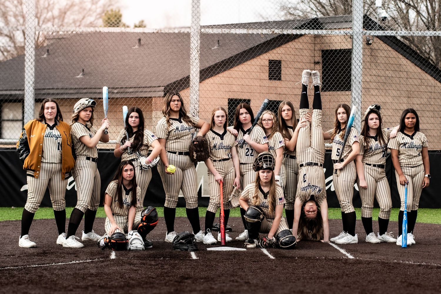 Girls softball team posing together outdoors on a field in matching uniforms.