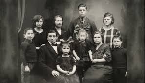 Vintage black and white family portrait photo with parents and children posed formally in early 20th century clothing.