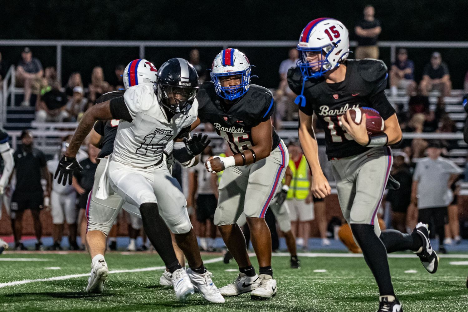 High school quarterback scrambling with ball past defenders at night.