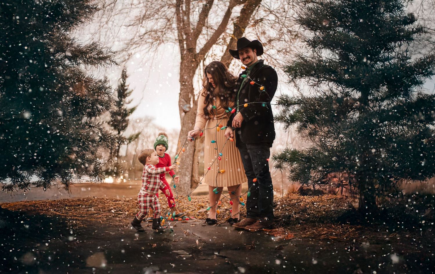 Family of three enjoying a magical snowy evening outdoors surrounded by festive pine trees.