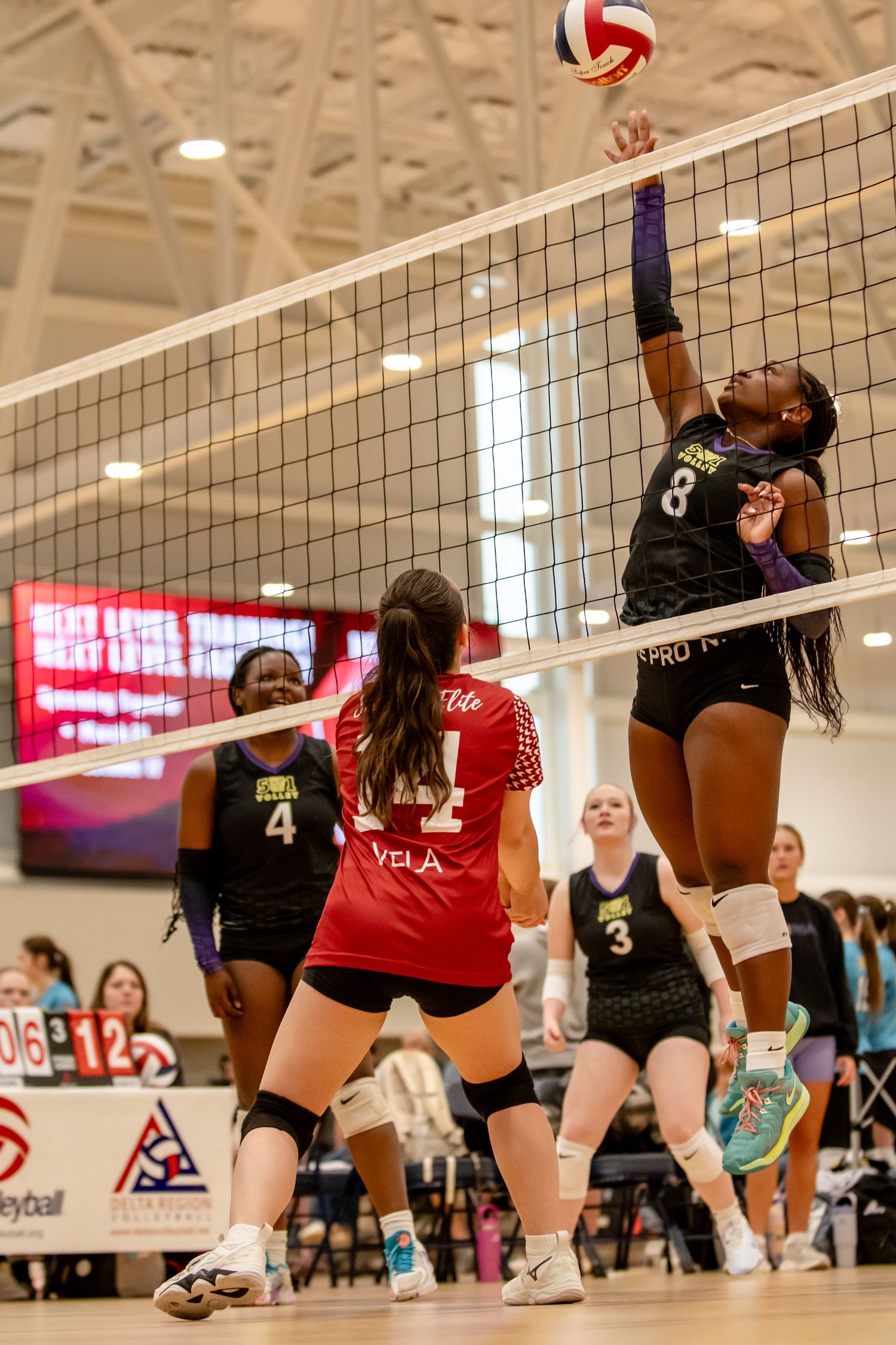 Volleyball player #8 jumps to spike the ball over the net during an indoor tournament match.