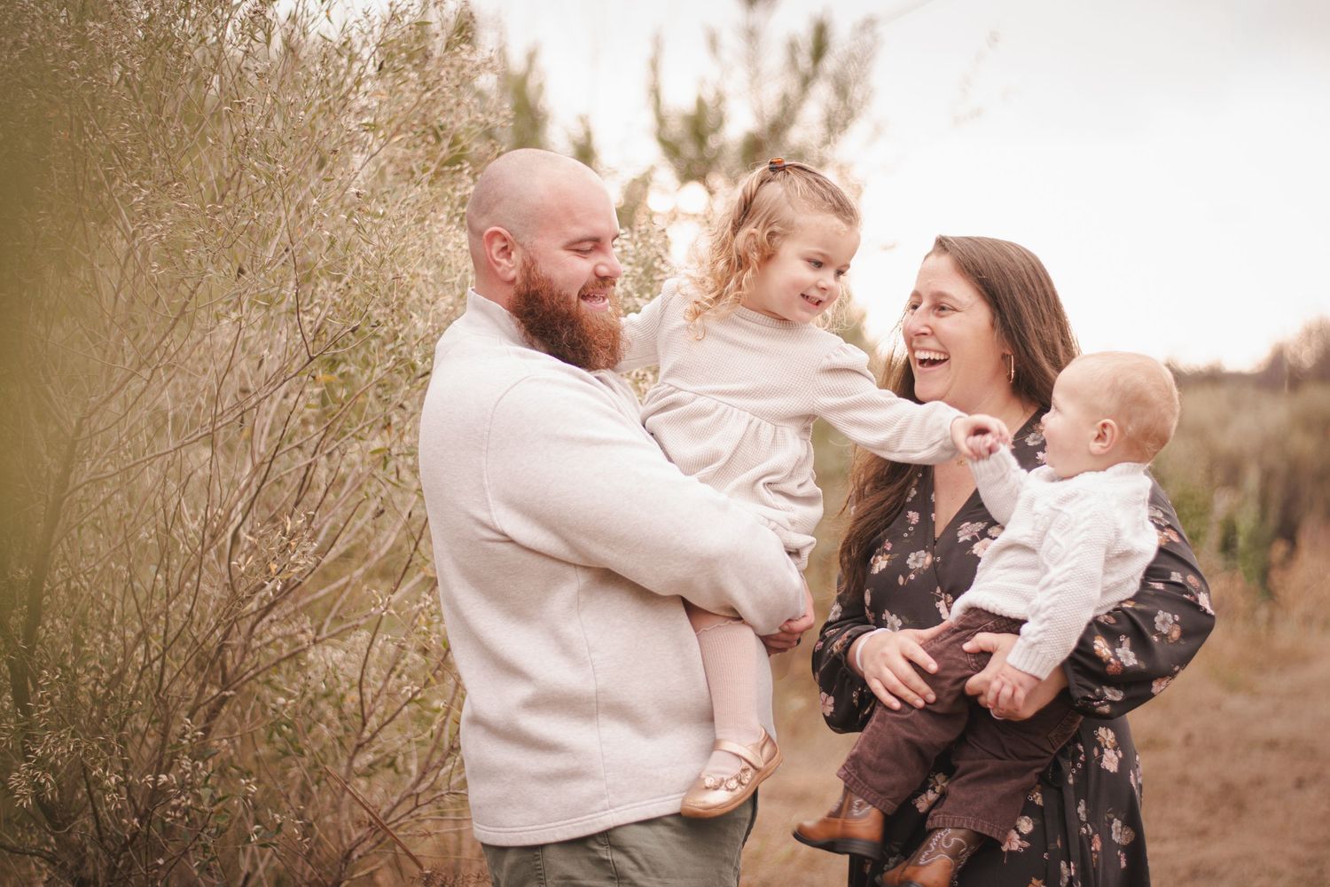 Happy family with two young children laughing outdoors in a natural field setting during golden hour.