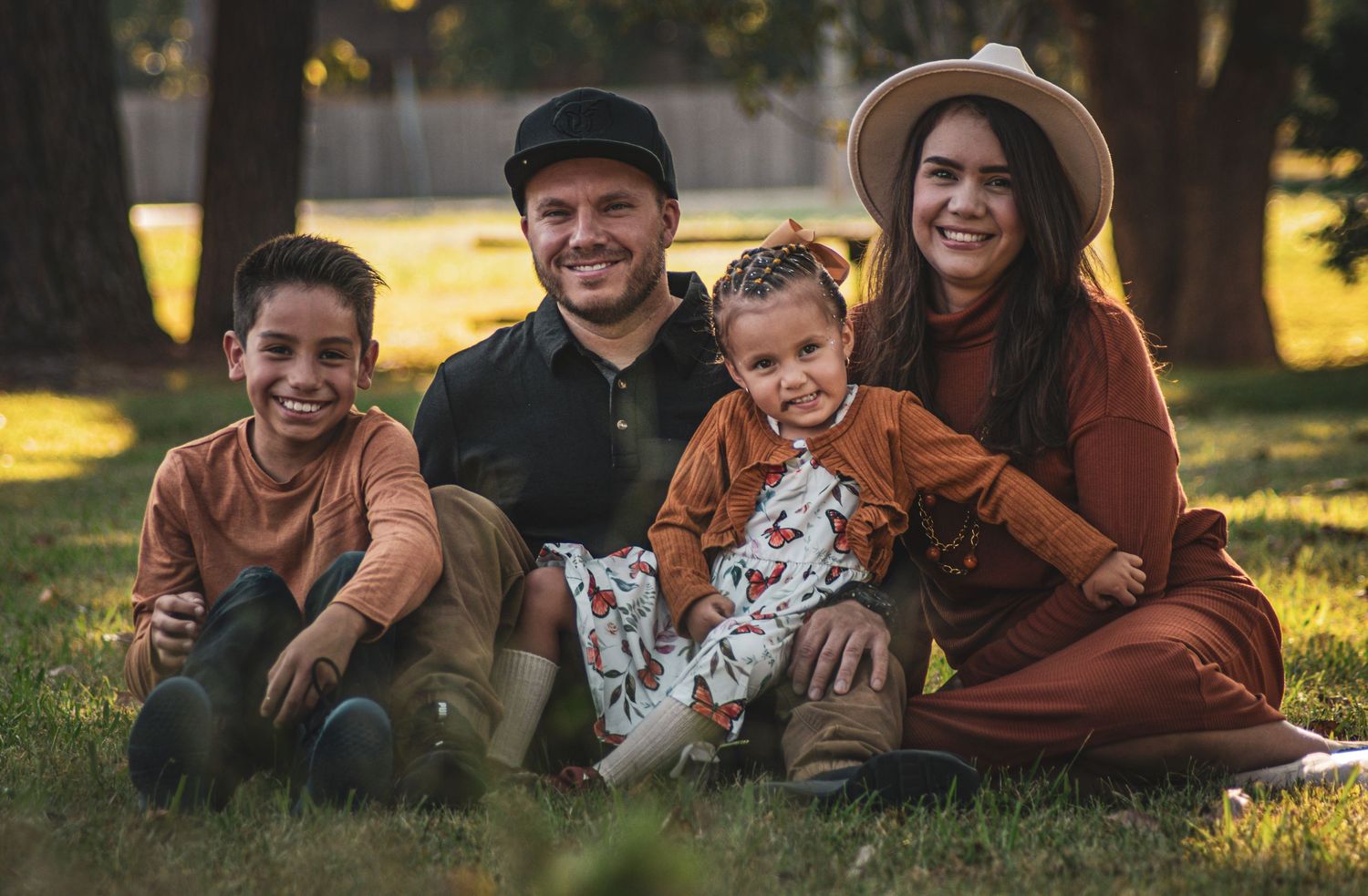 Happy family of four sitting together on green grass in a sunny park.