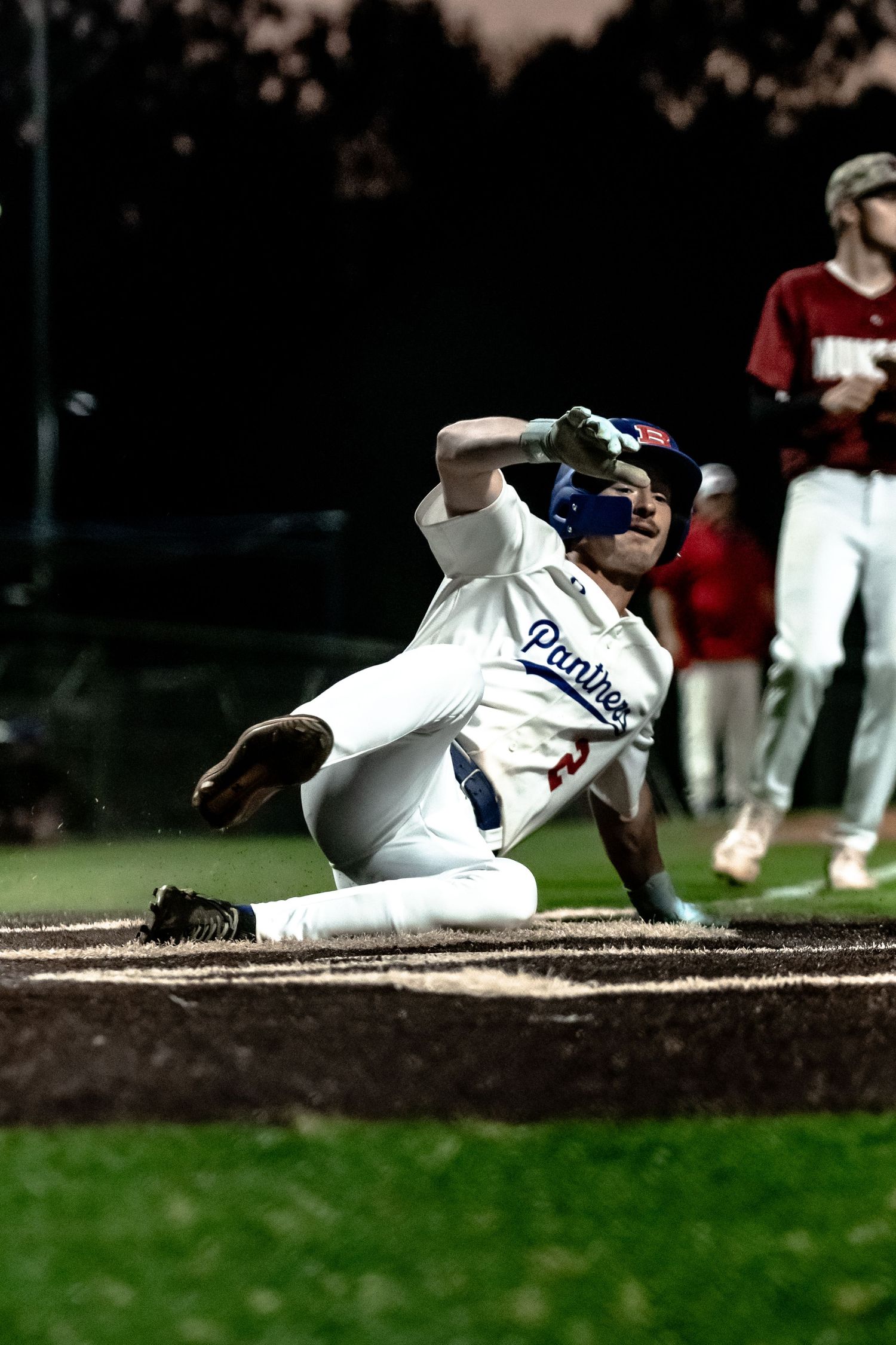 Baseball player in white Panthers uniform sliding into base during a night game.