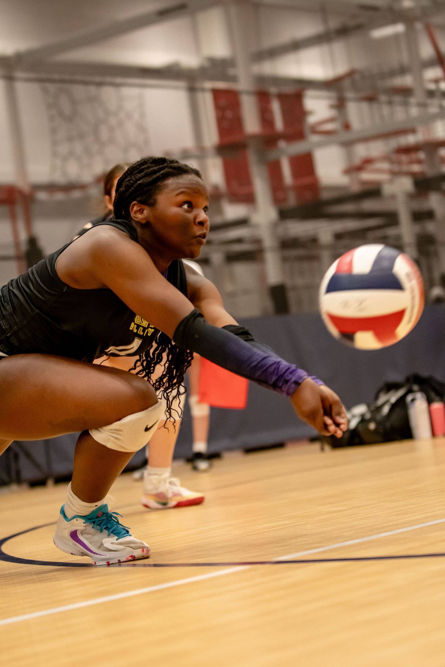 Female volleyball player digs a low ball during an intense indoor volleyball match.