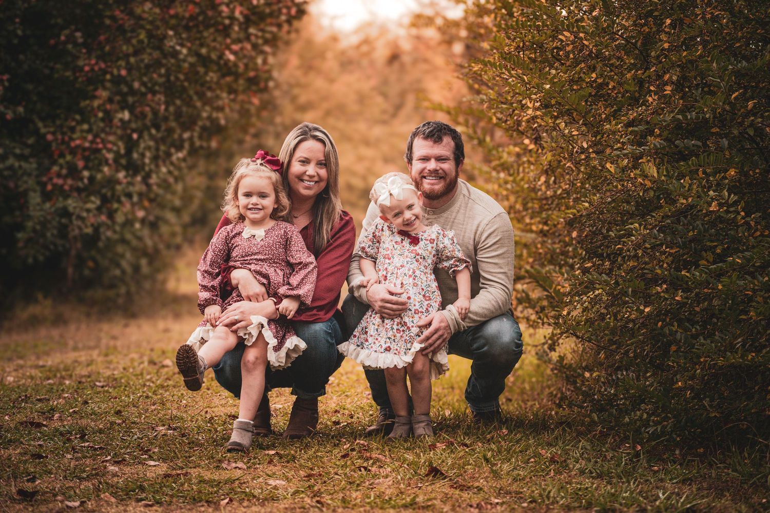 Happy family of four poses together among colorful autumn trees outdoors.