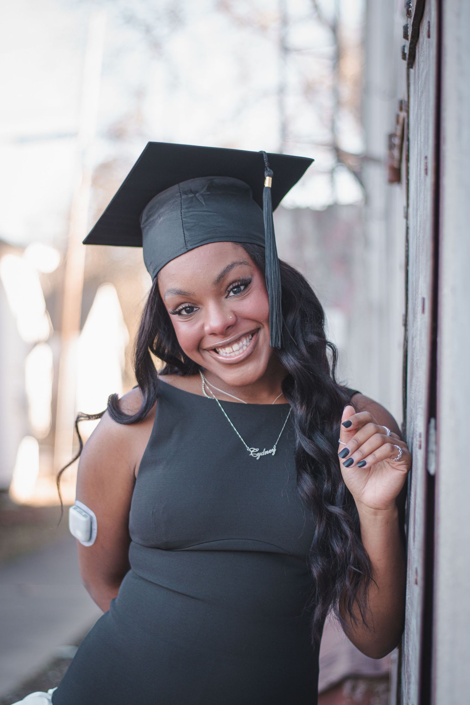 Senior Portrait Session. Smiling young woman in black graduation cap and dress celebrating her academic achievement outdoors.