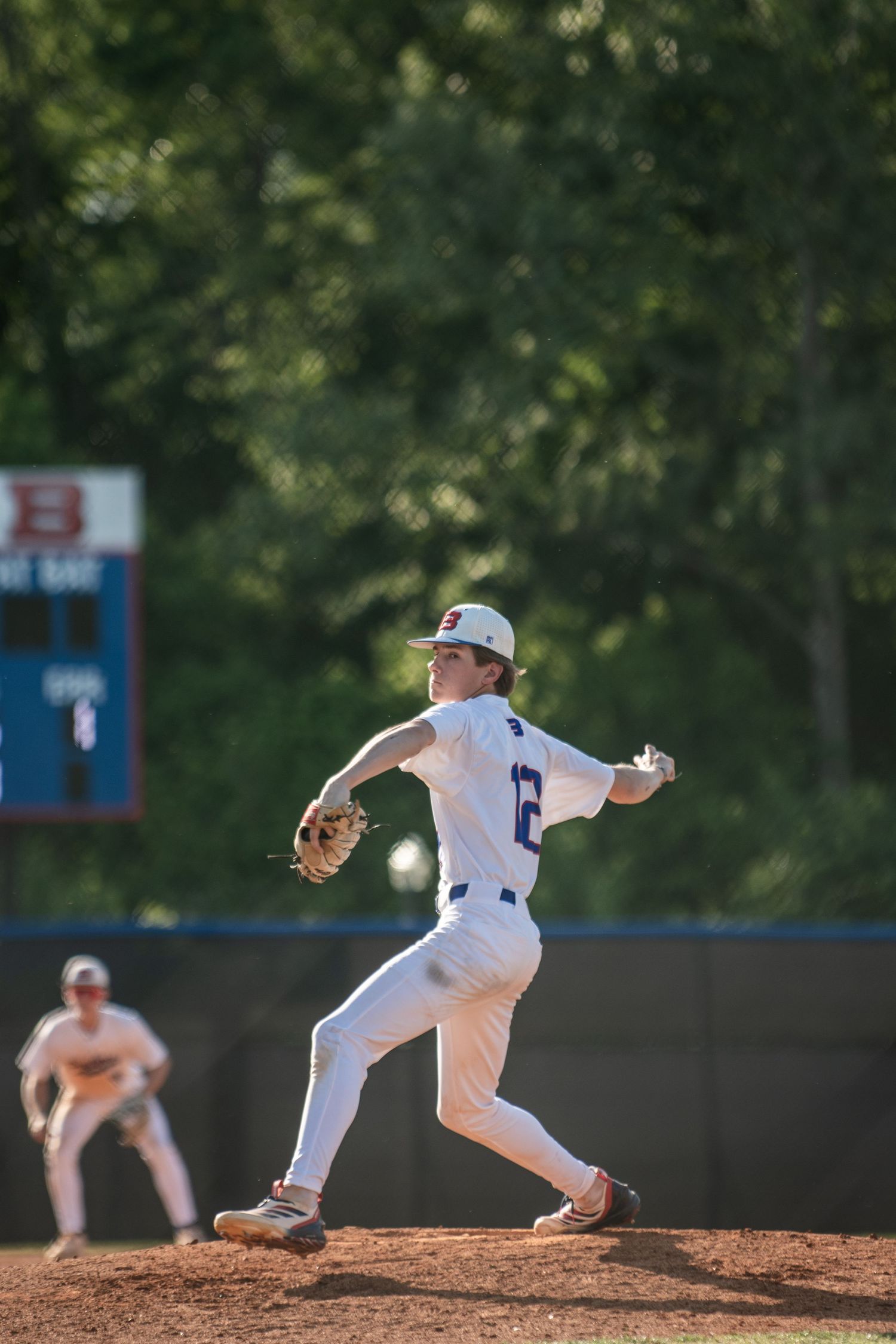 High school baseball pitcher winding up to throw on sunny mound.