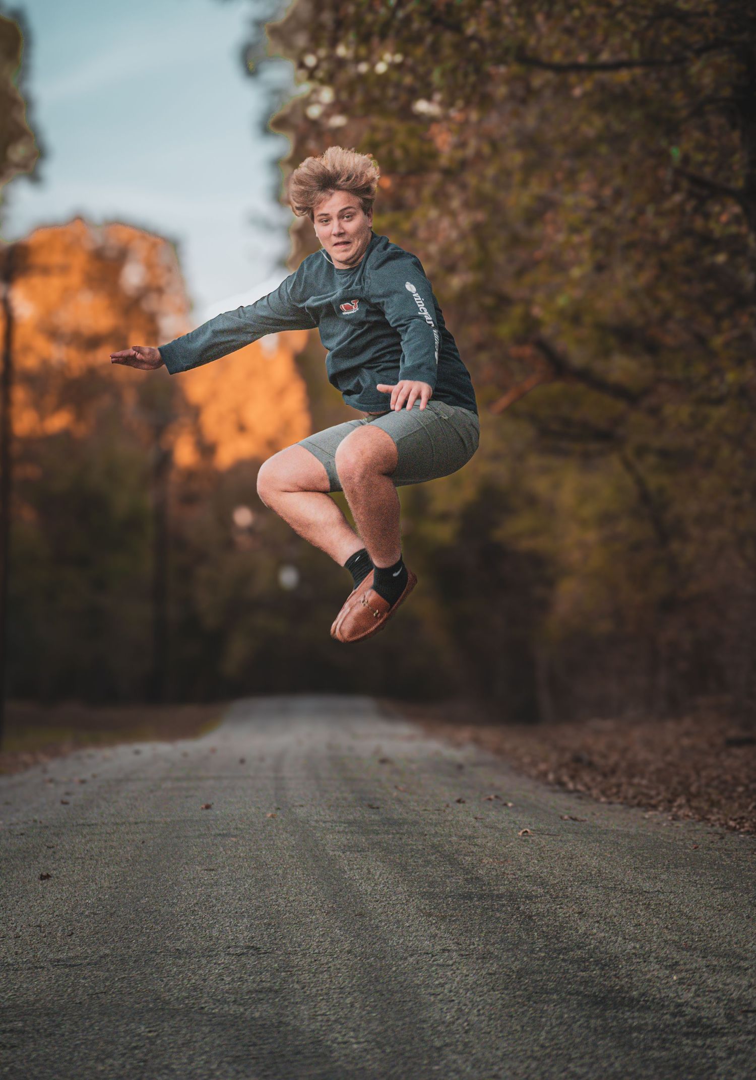 Teen boy jumps mid-air on rural road surrounded by autumn foliage.
