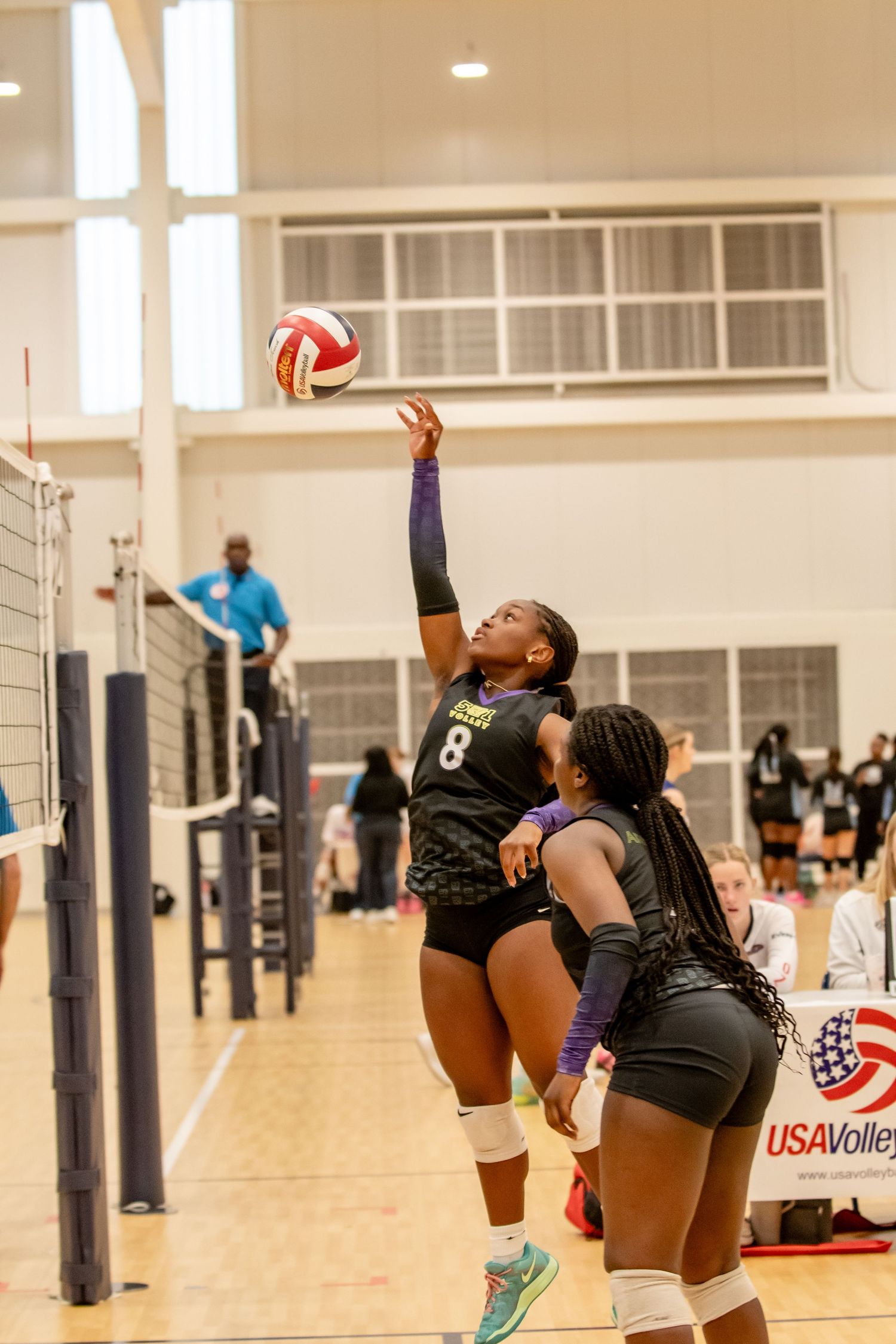 Player #8 spikes volleyball at USA Volleyball indoor tournament while teammate watches during competitive match.