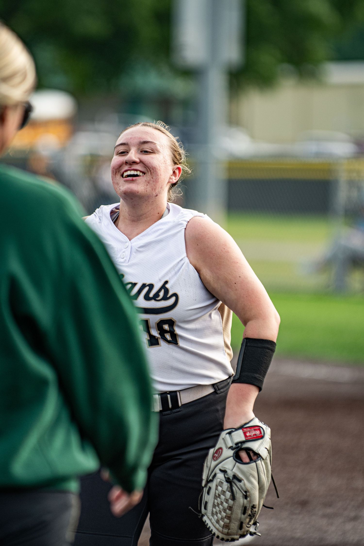 Smiling softball player in white jersey holding glove during a game.