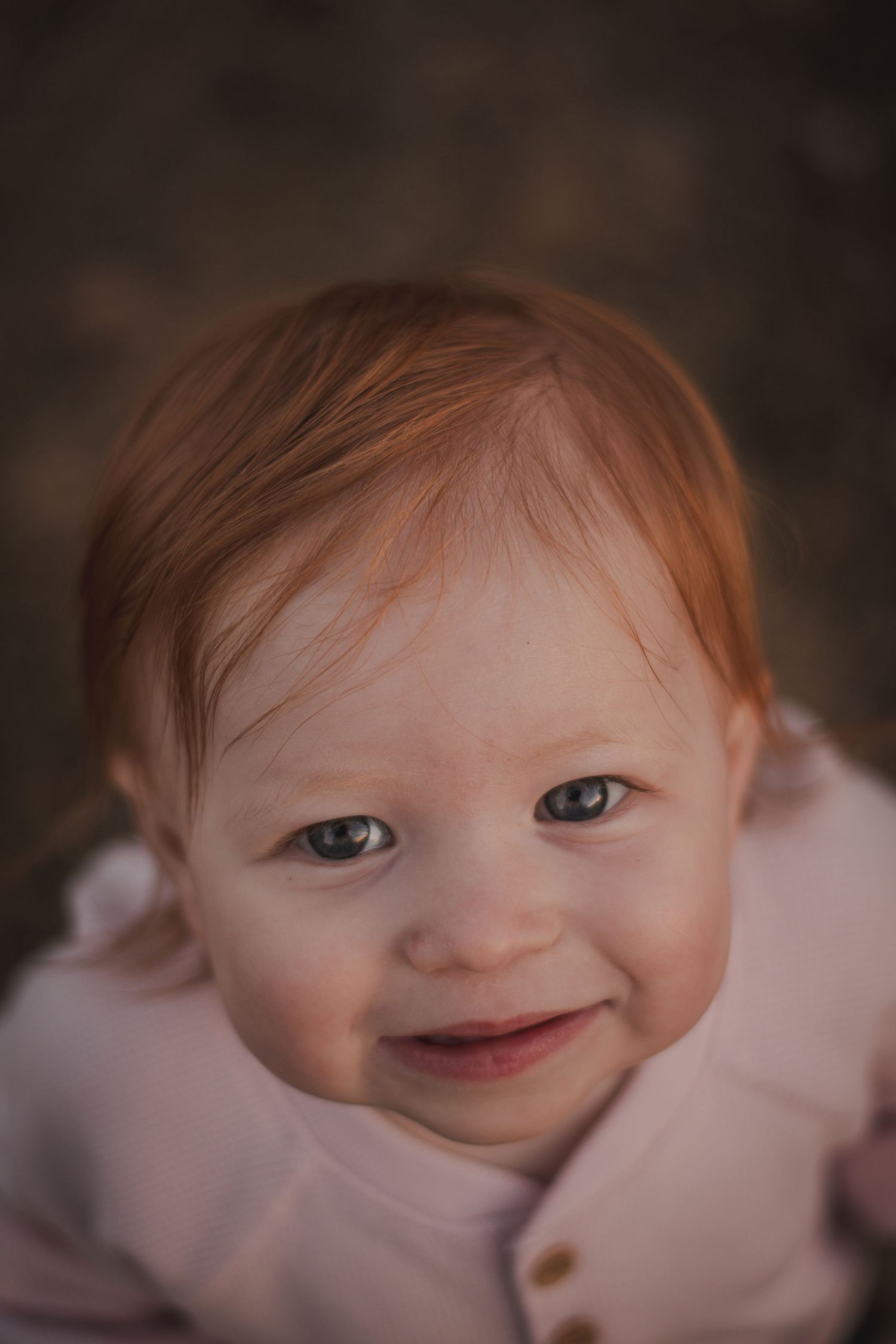Adorable red-haired baby with blue eyes smiles in close-up portrait.