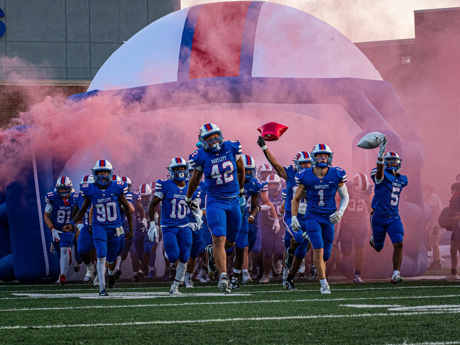 High school football team runs onto the field through colorful smoke during a dramatic entrance.