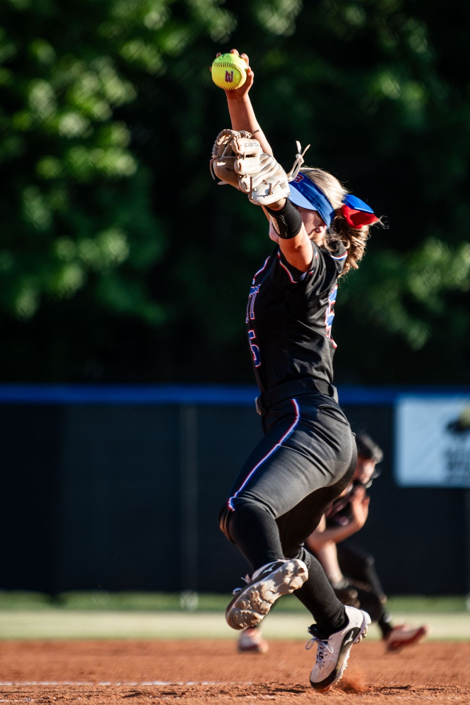 Female softball pitcher leaping mid-air during dynamic windmill pitch.