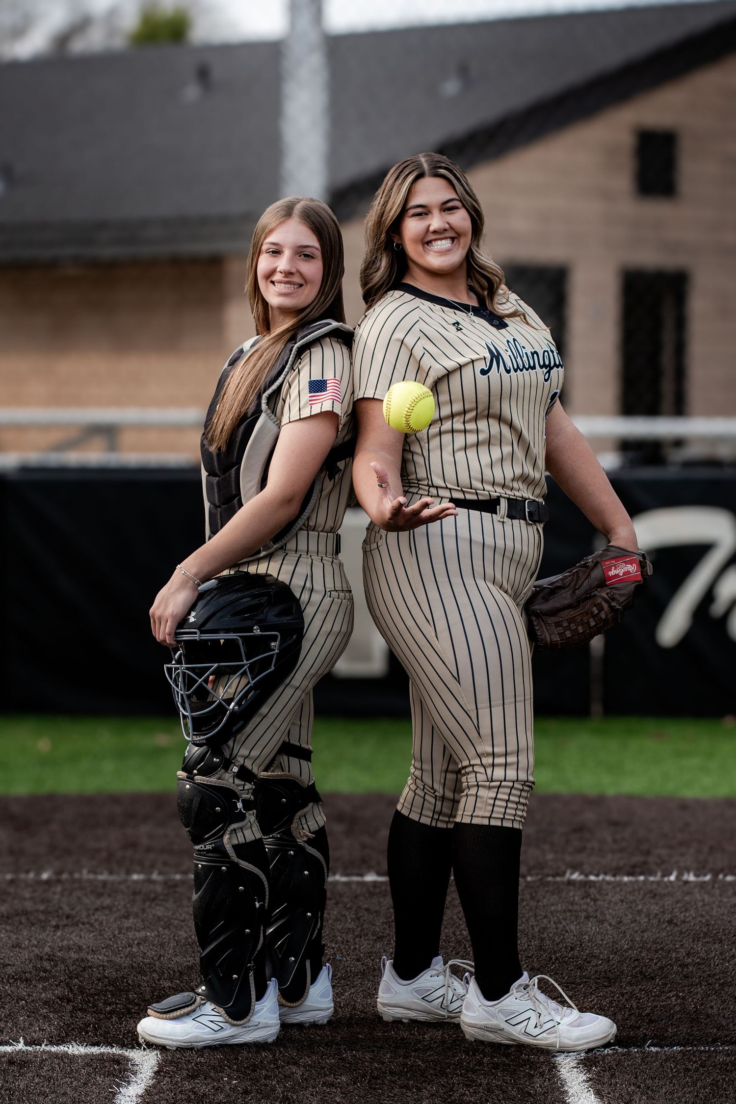 Two female softball players in Millington uniforms posing with catcher gear and glove.