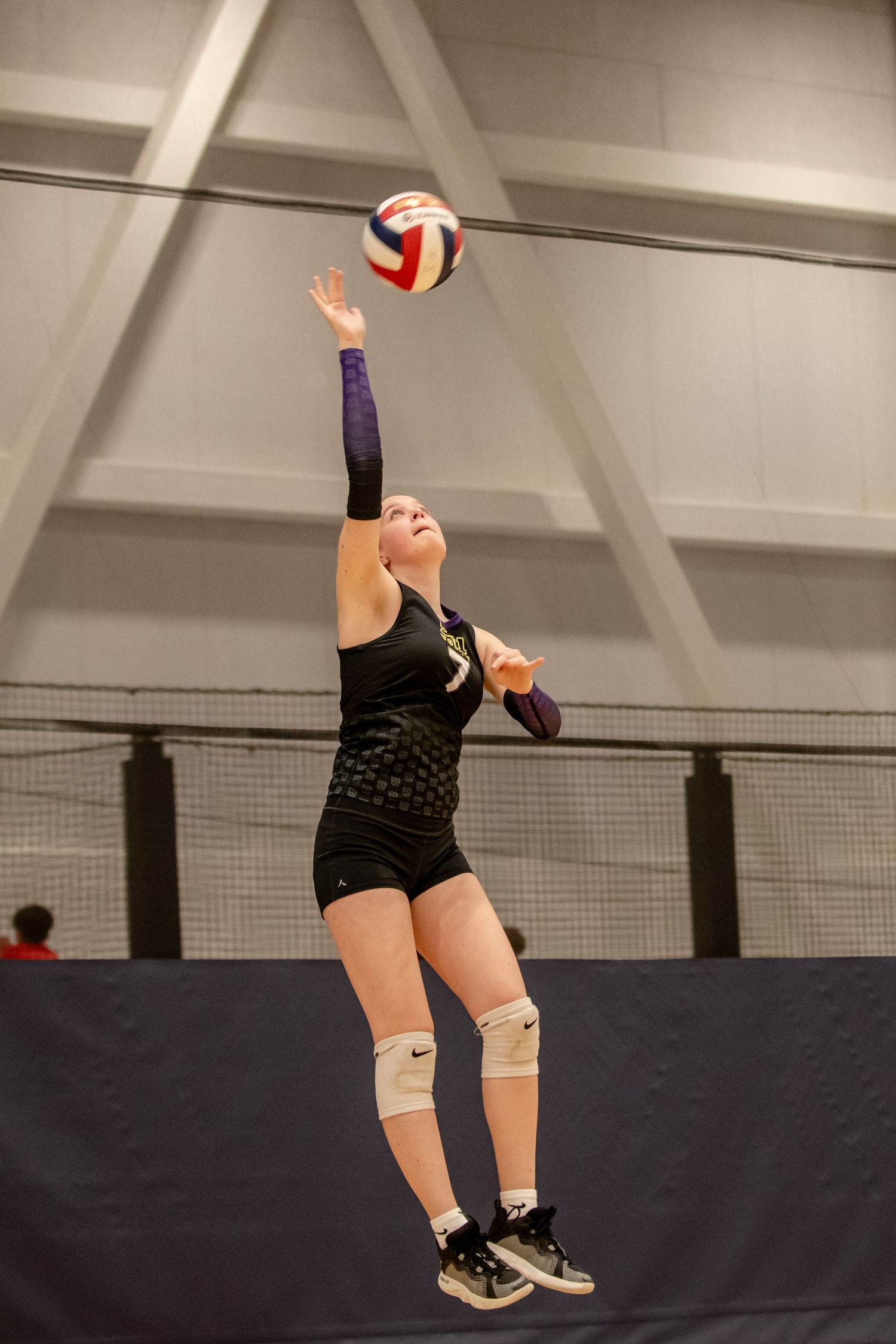 Female volleyball player jumps to serve the ball during an indoor volleyball tournament.