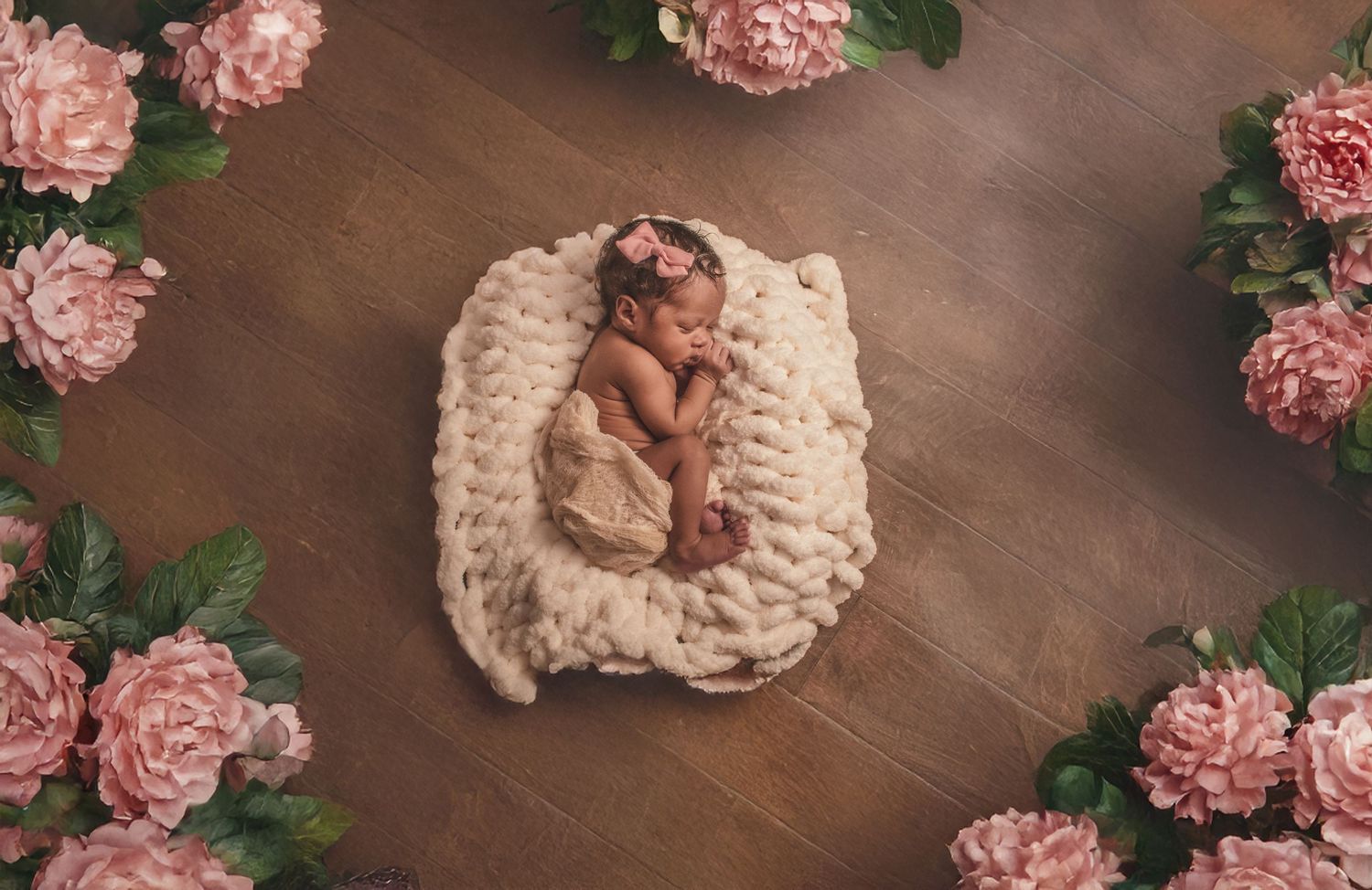 Sleeping newborn baby on cream knit blanket surrounded by pink flowers.
