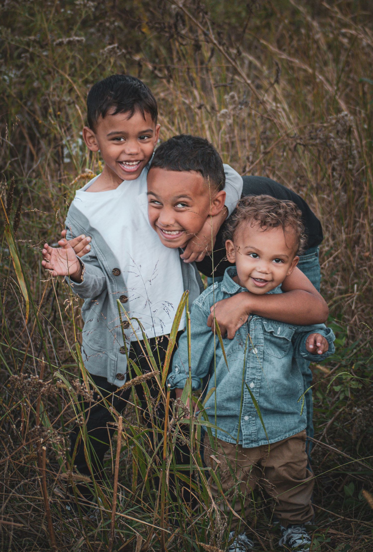 Three happy young brothers hugging and smiling together in a grassy outdoor field.