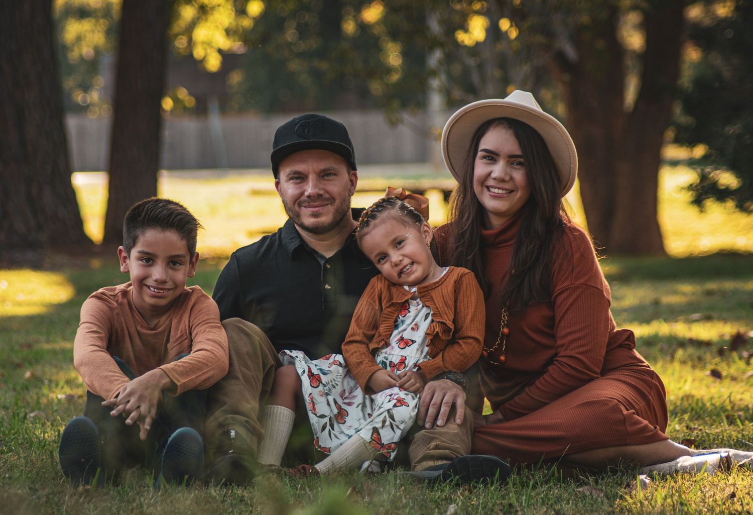 Happy family of four sitting together on green grass in sunny park setting.