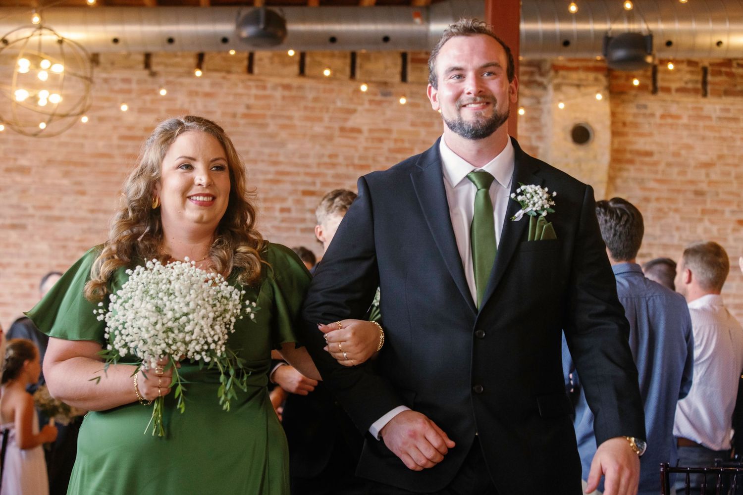 Wedding party members walking down aisle holding baby's breath bouquets in industrial venue.