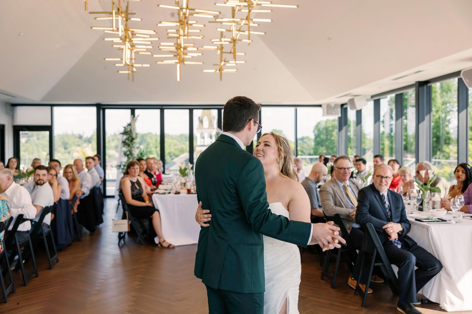 Modern reception venue with chandeliers and large windows overlooking greenery.