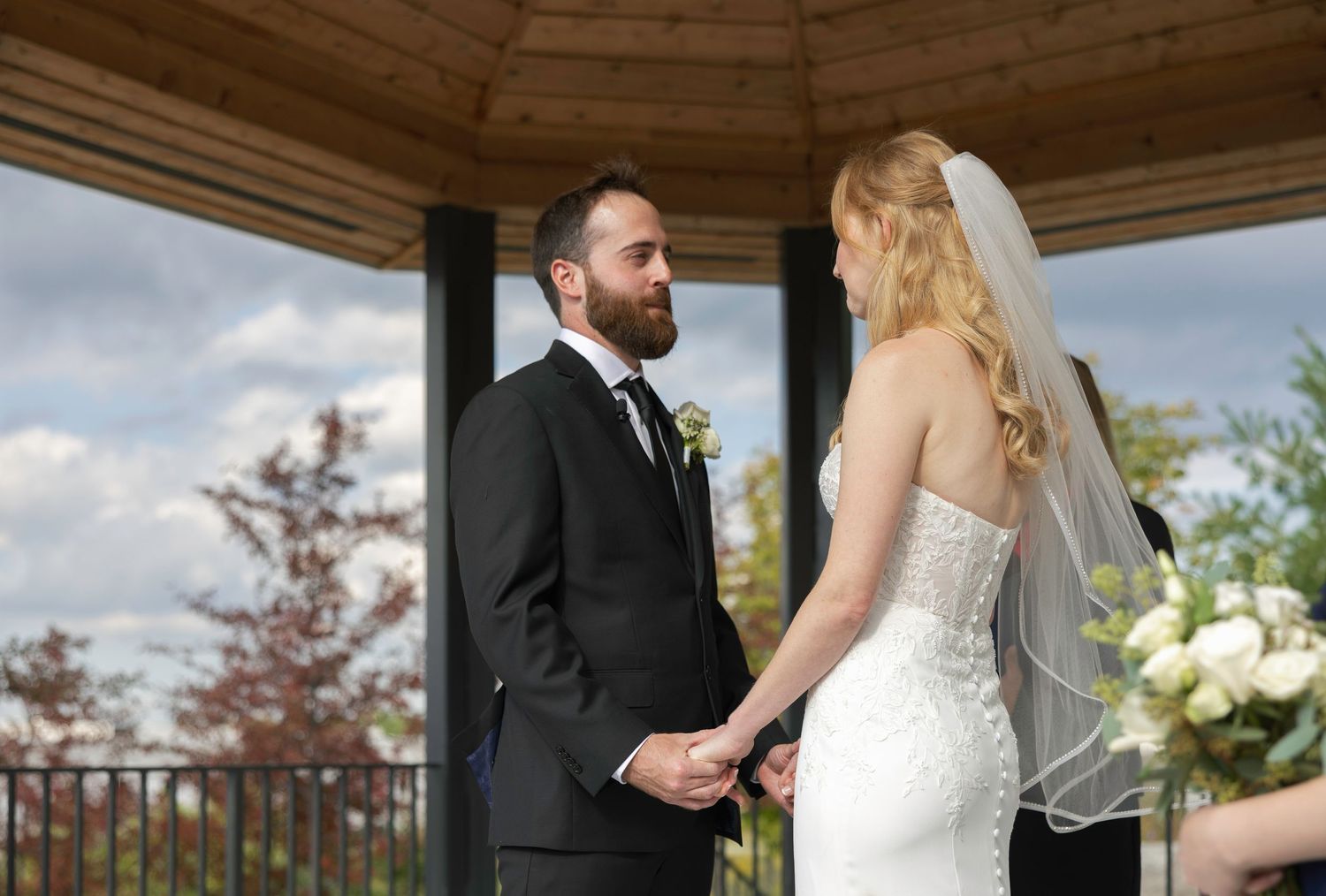 A couple shares an intimate moment during their outdoor wedding ceremony under a wooden gazebo.