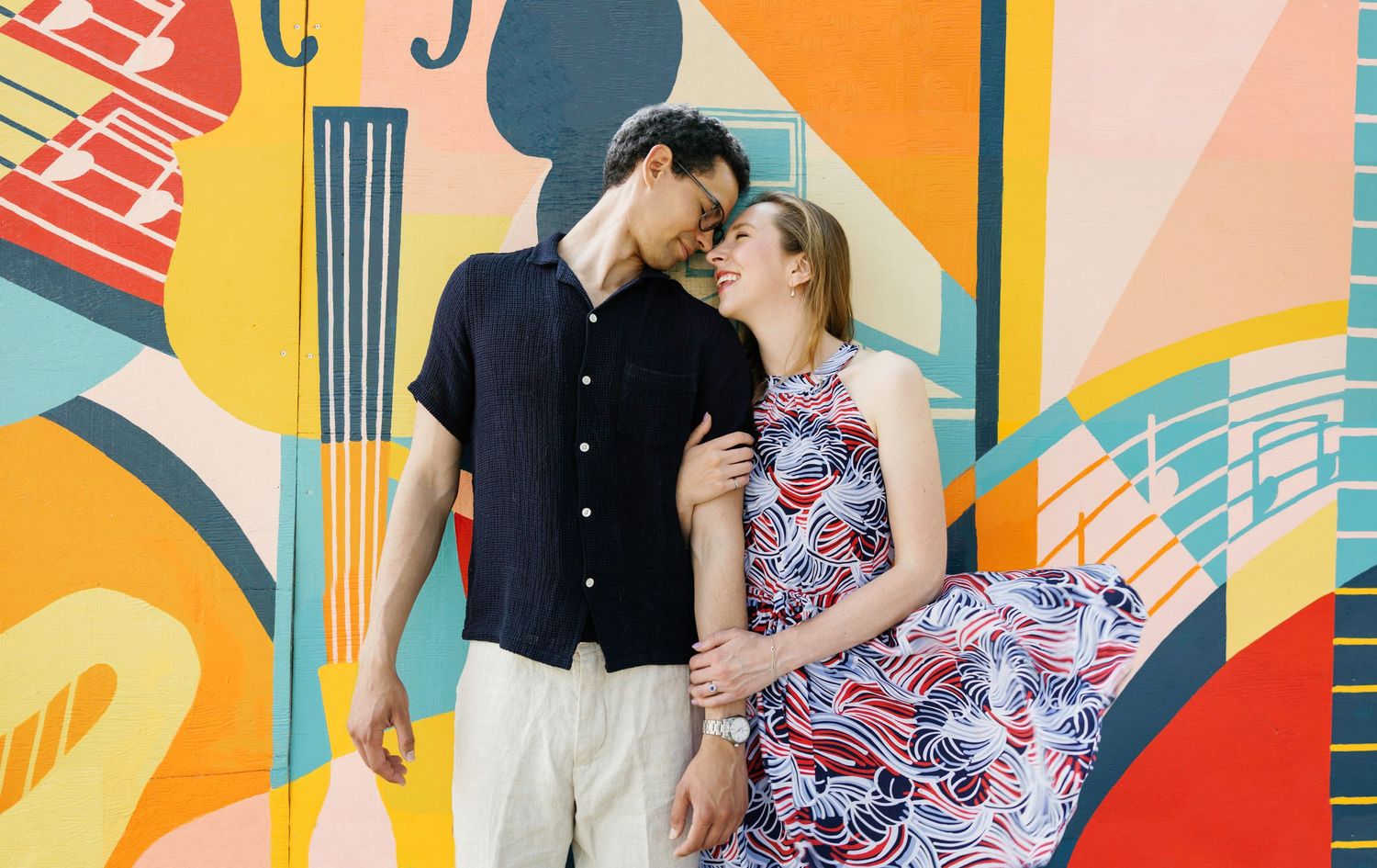 Couple poses against vibrant colorful geometric mural wall during engagement photo session.