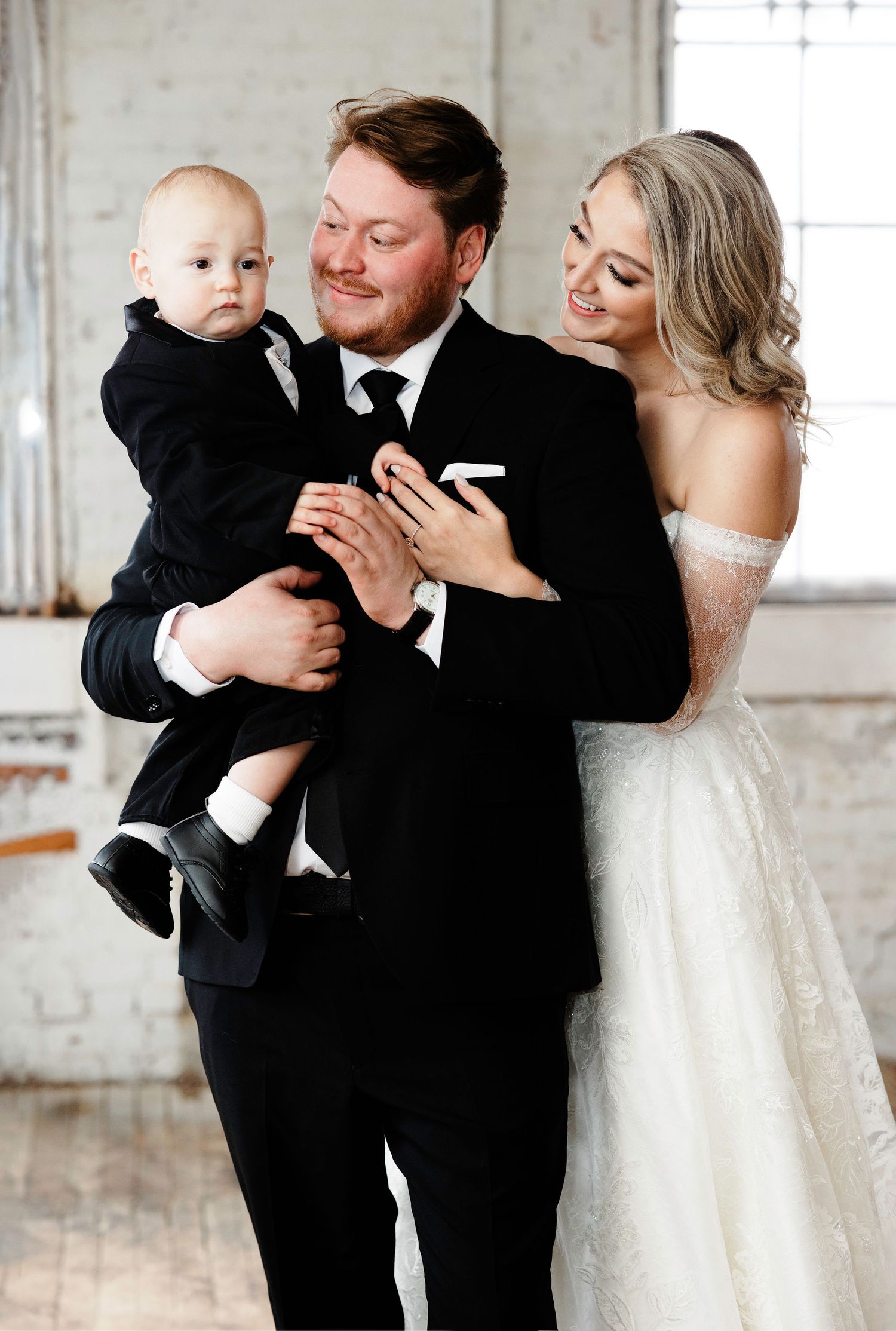 Wedding couple shares joyful moment with small child in formal attire.