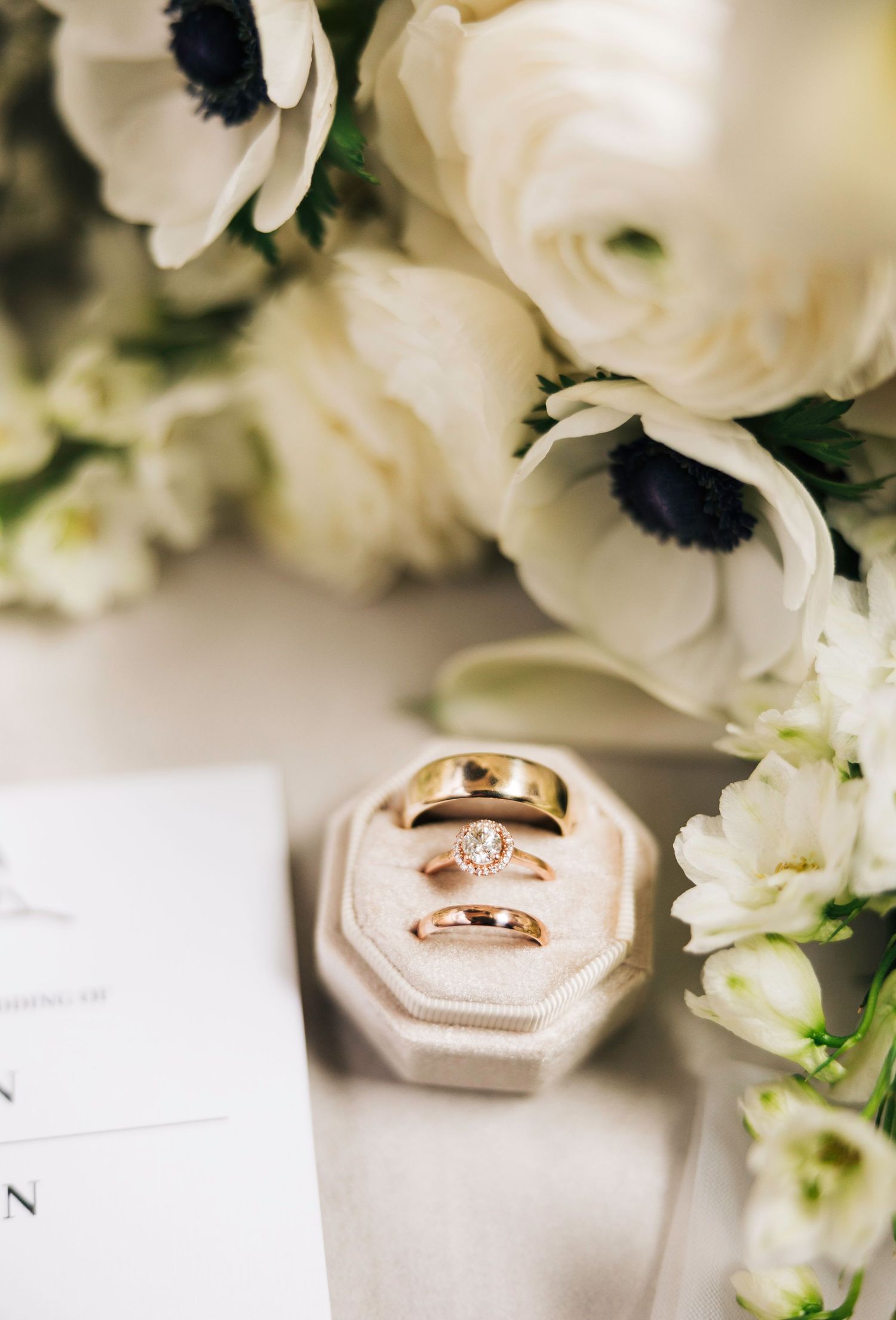 Wedding rings nestled in a white velvet ring box surrounded by delicate white anemone flowers and floral arrangements.